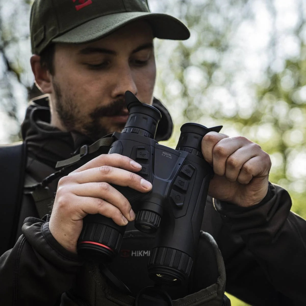 Una persona ajusta un binocular multiespectral Hikmicro HQ35L 5.5-22x60 sostenido a la altura del pecho, en terreno.